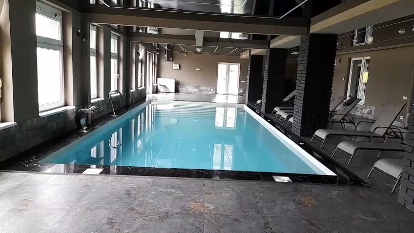 Piscină interioară cu apă turcoaz, ferestre mari și șezlonguri.