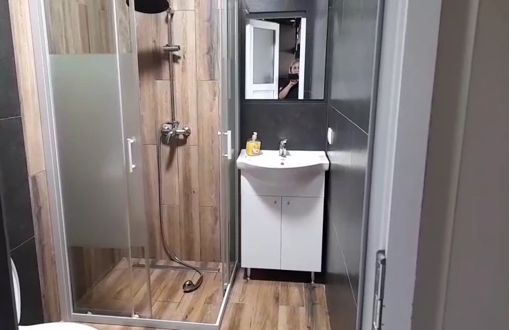 Baie modernă cu duș din sticlă, finisaje din lemn și lavoar alb.