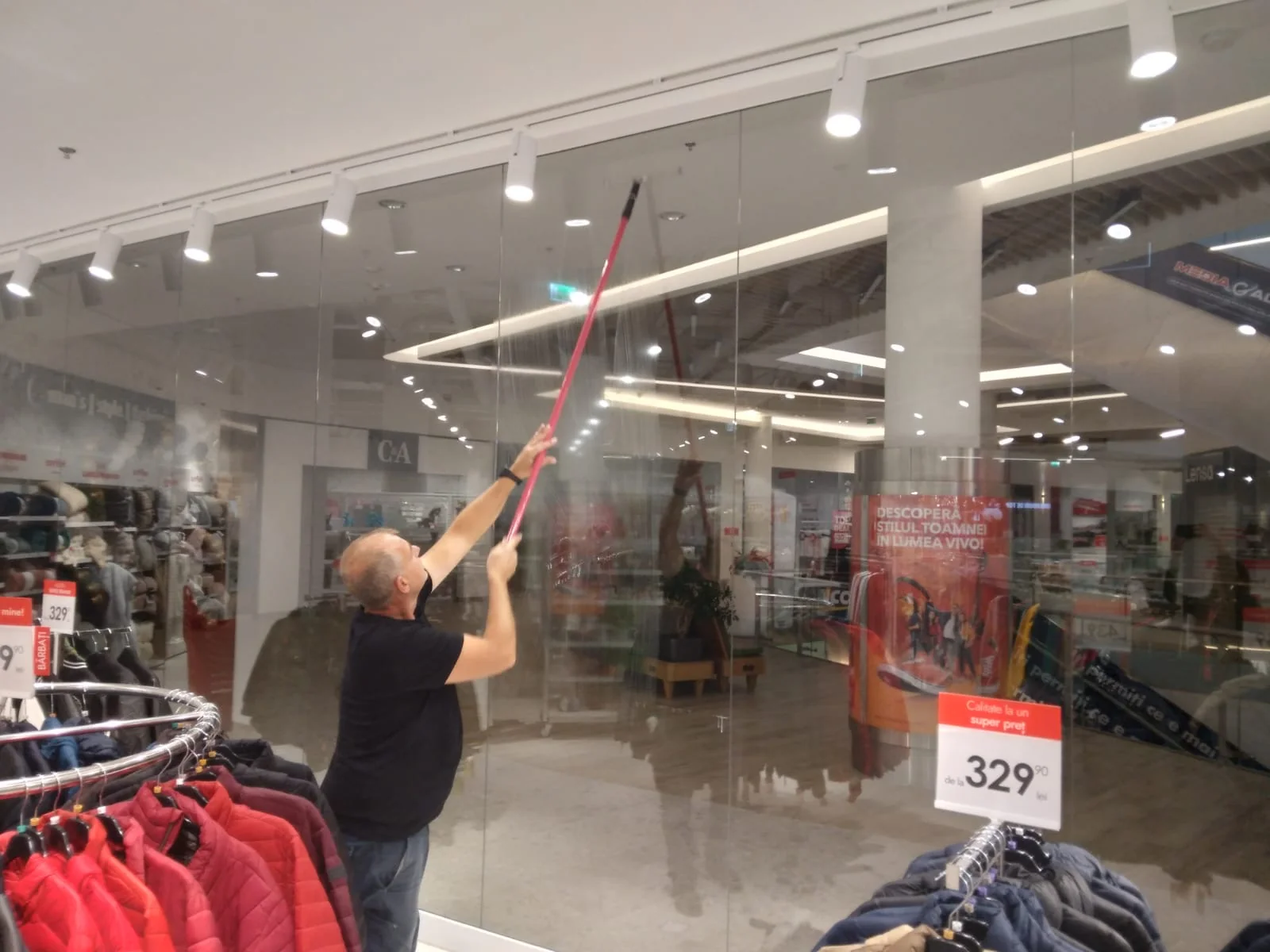 Curățarea unei vitrine de magazin cu un dispozitiv telescopic.